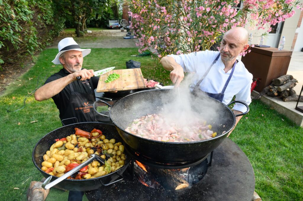 Deux chefs cuisinent au brasero dans un jardin fleuri