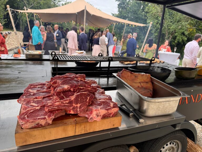 Côtes de bœuf crues sur une planche, prêtes pour le brasero, invités en arrière-plan