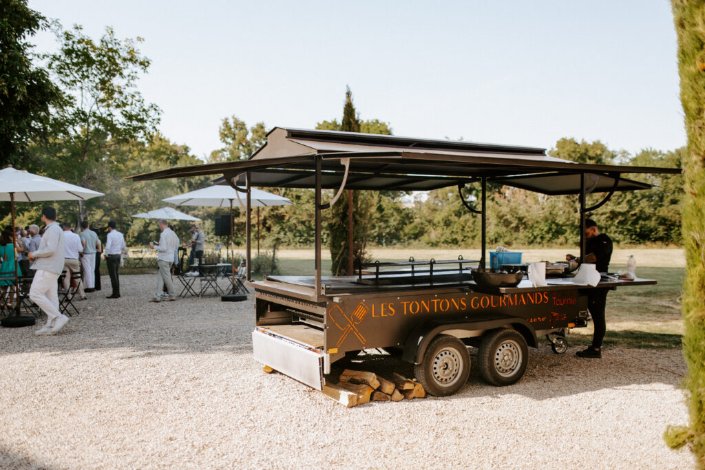 La remorque tourne-broche des Tontons Gourmands dans le parc d’un domaine, invités autour