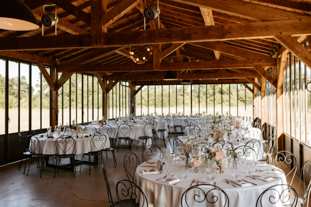 Tables rondes dressées sous une grande halle en bois, pour un mariage